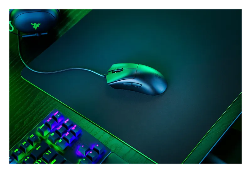 Razer DeathAdder V3 mouse on a mouse pad lit in green next to a keyboard