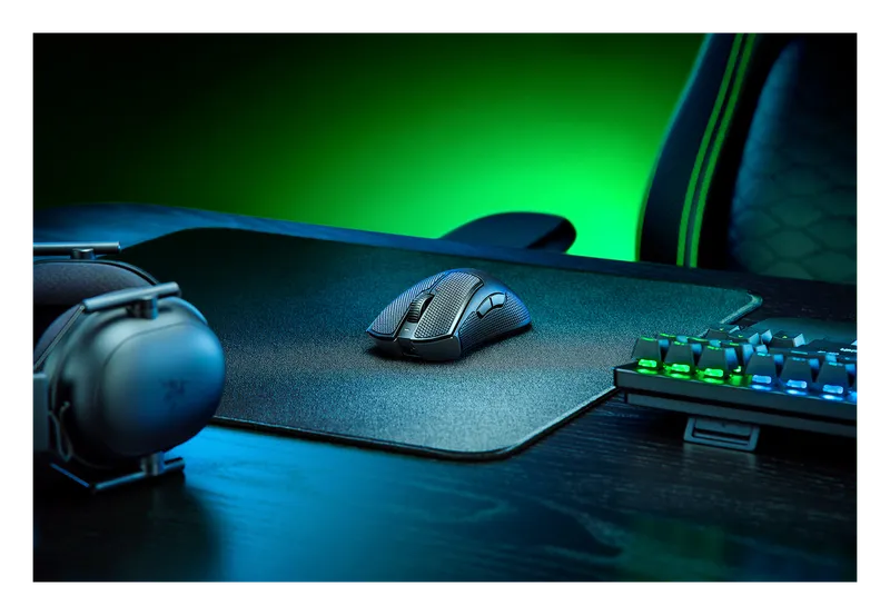 Razer DeathAdder V3 Pro mouse on a desk with a green-lit keyboard