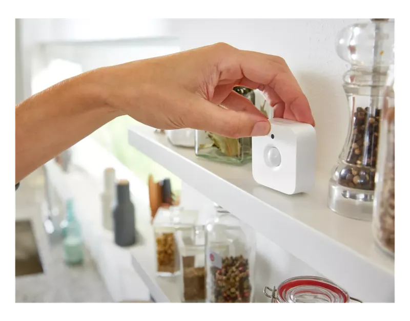 Hand placing a Philips Hue Motion Sensor on a kitchen shelf